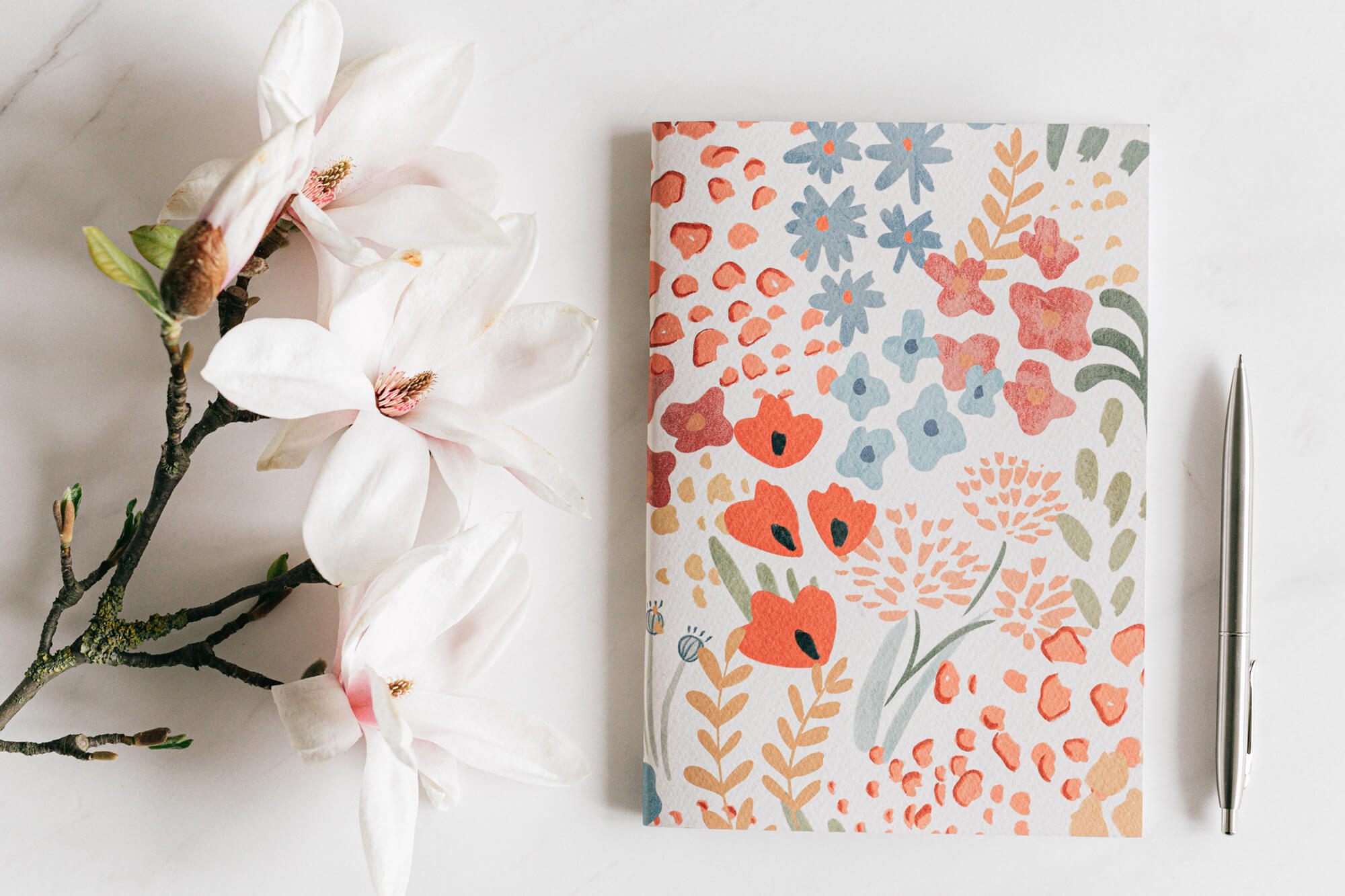 A floral theme notebook next to white flowers and a pen