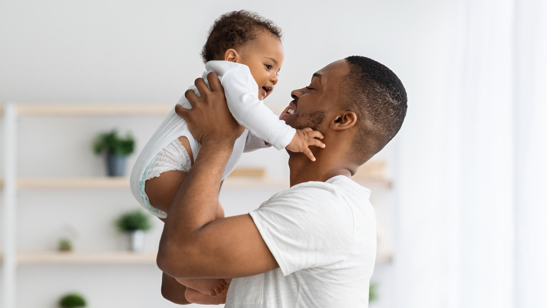 A man lifts his baby up close to his face. Both are wearing white.