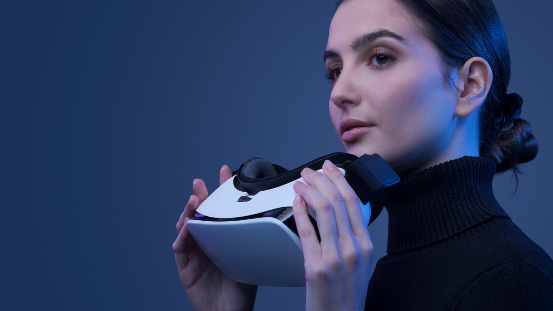 A woman in a black turtleneck holds white virtual reality goggles