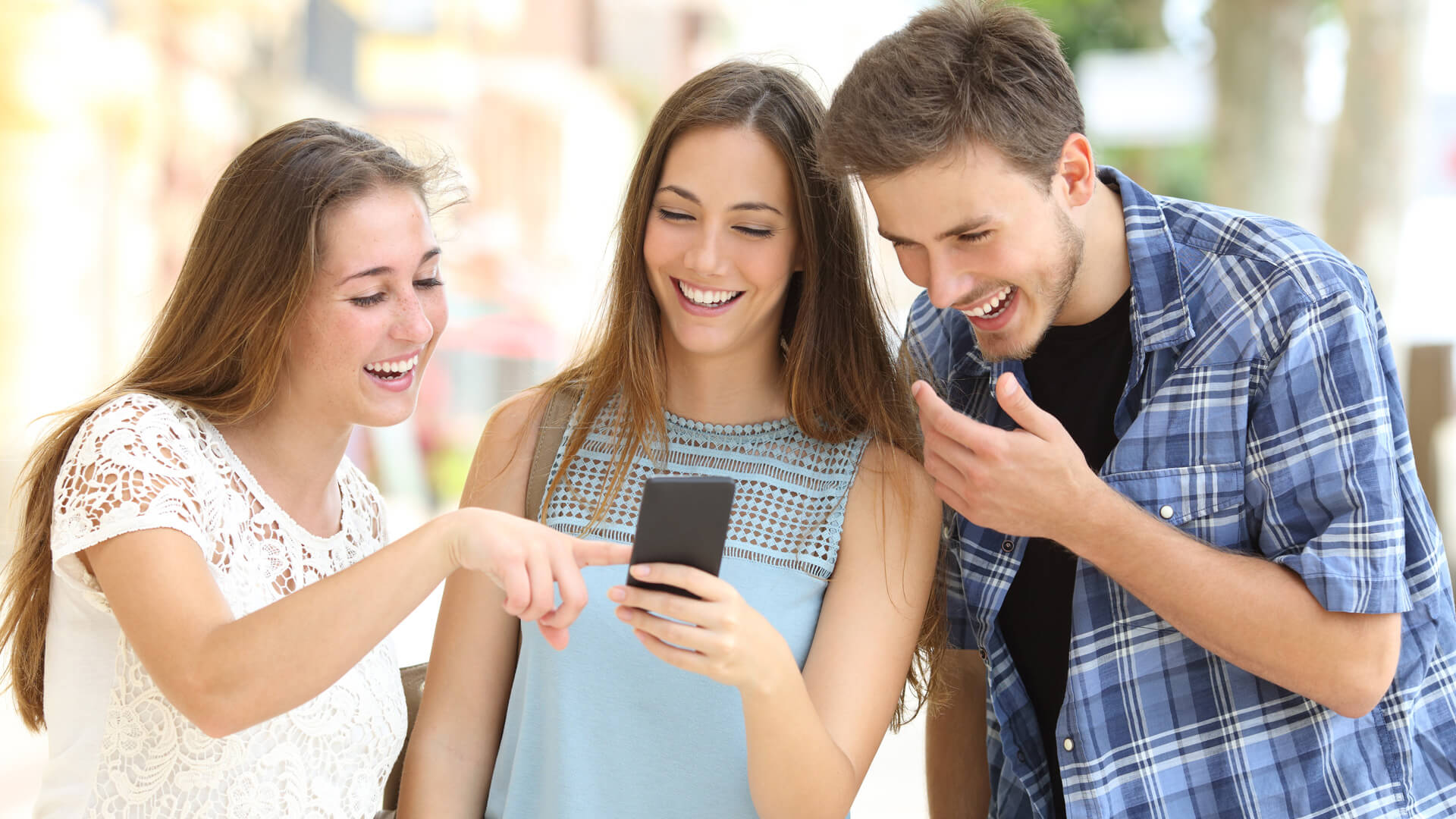 Two women and a man laugh as they look at a phone