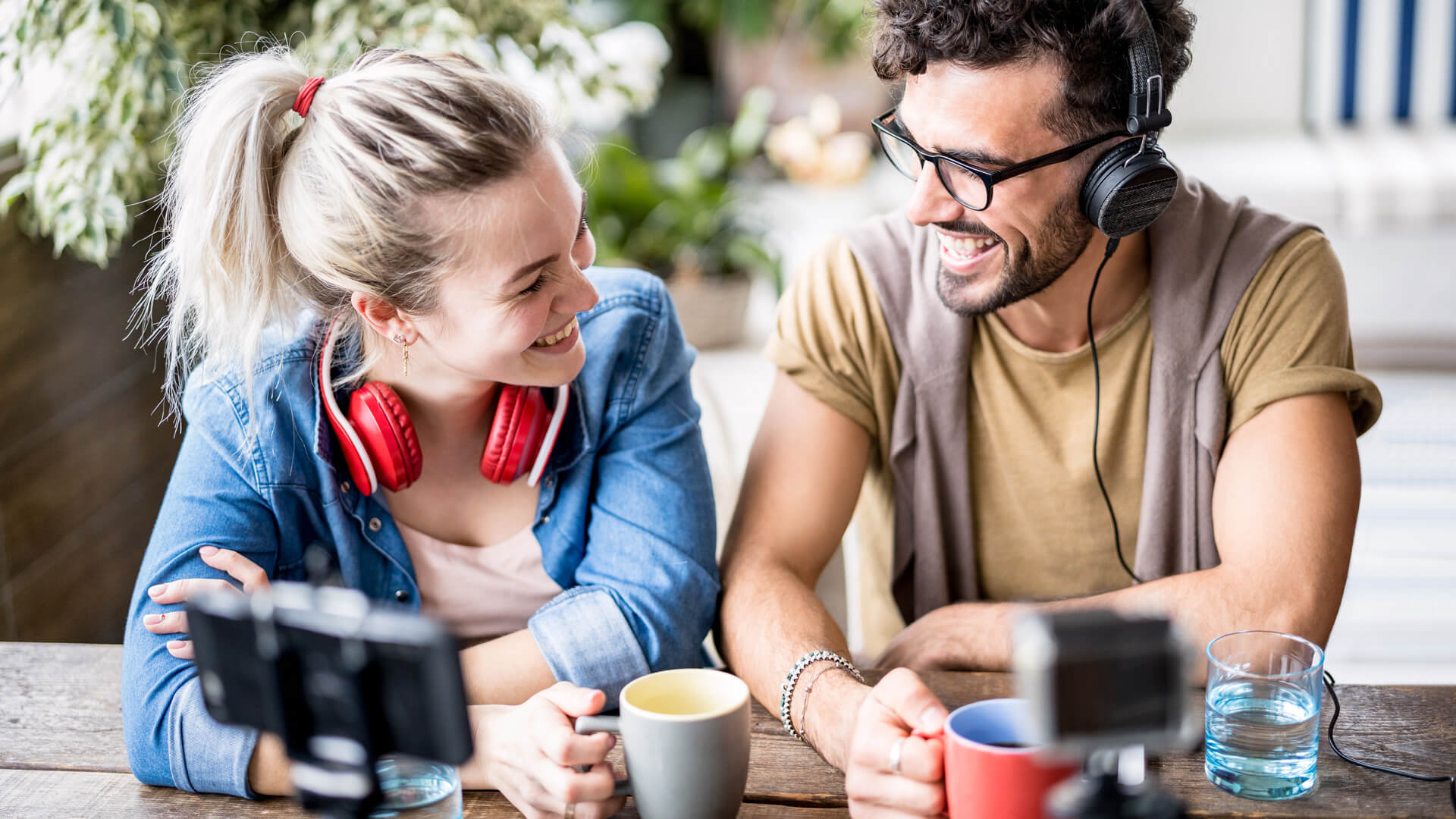 A woman with blonde hair in a ponytail and red headphones over her neck and a man wearing black glasses with dark, curly hair