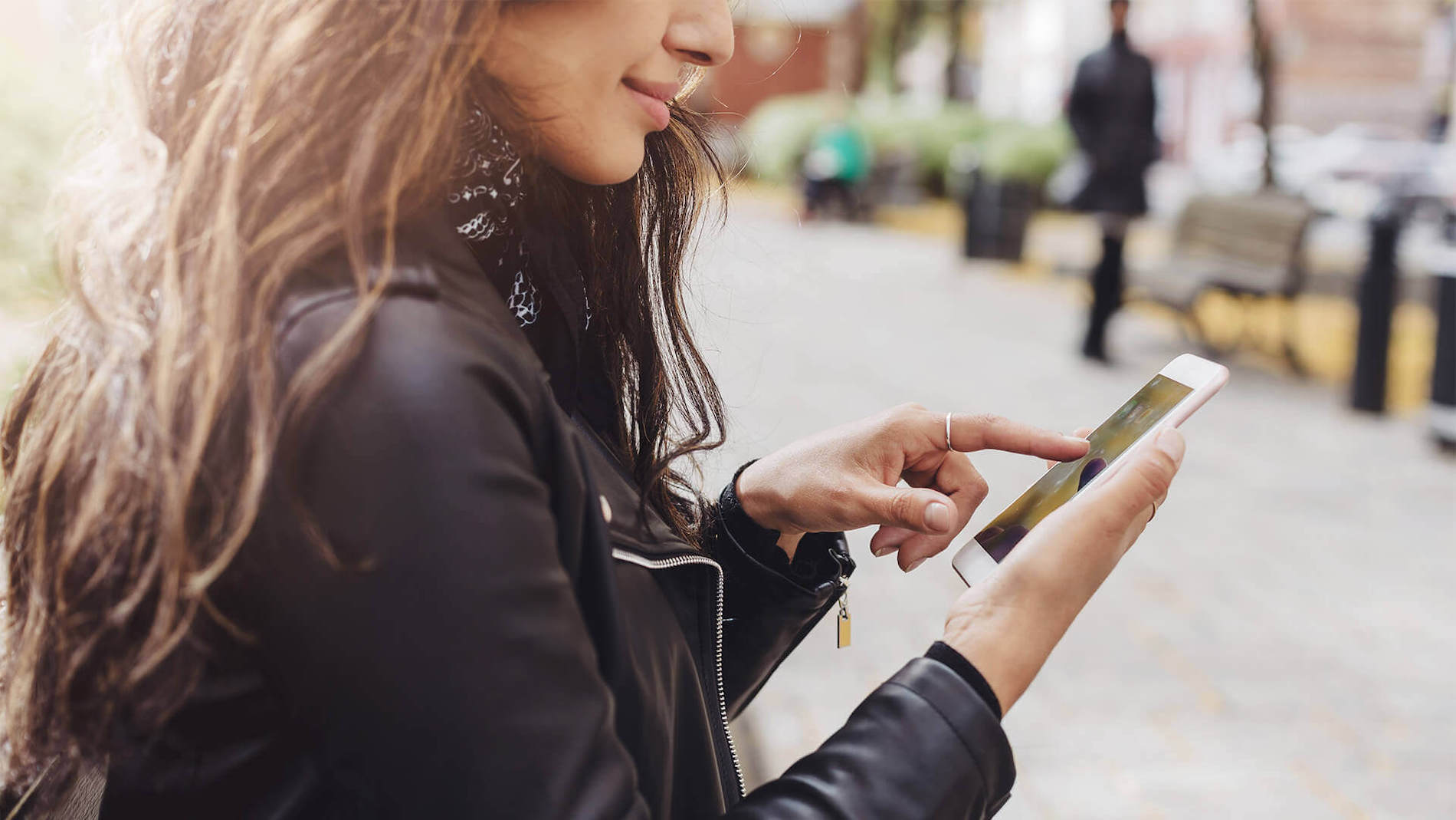 A woman with long brown hair and a black leather jacket looks on her phone